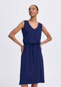 Navy blue sleeveless dress with a V-neck and drawstring waist. Made of soft fabric, it has a relaxed fit and falls just below the knee.