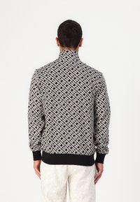 Černobílá mikina s vysokým límcem, elastickými manžetami a páskem, zdobená geometrickým vzorem na měkké tkanině.