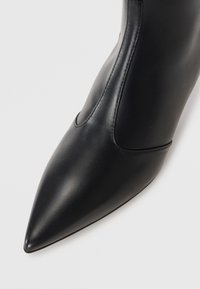 Bottine noire en cuir avec un bout pointu, au toucher lisse, au design élégant et à la cheville ajustée. Présente une couture minimale et une semelle de couleur unie.