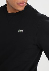 Sudadera negra hecha de una mezcla de algodón, con un escote redondo y un pequeño logo de cocodrilo bordado en verde en el pecho.