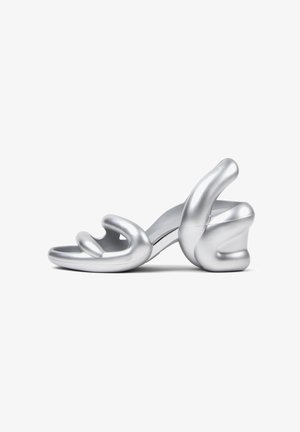 Silberner High-Heel-Sandal mit einem geformten Design, das gebogene Riemen und einen klobigen, skulpturalen Absatz aufweist. Glatte, metallische Oberfläche.