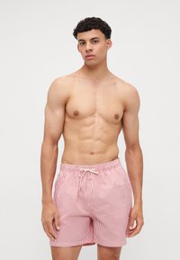 Κόκκινα και λευκά ριγέ μαγιό από ελαφρύ ύφασμα, με ελαστική μέση και κορδόνι για ρυθμιζόμενη εφαρμογή.