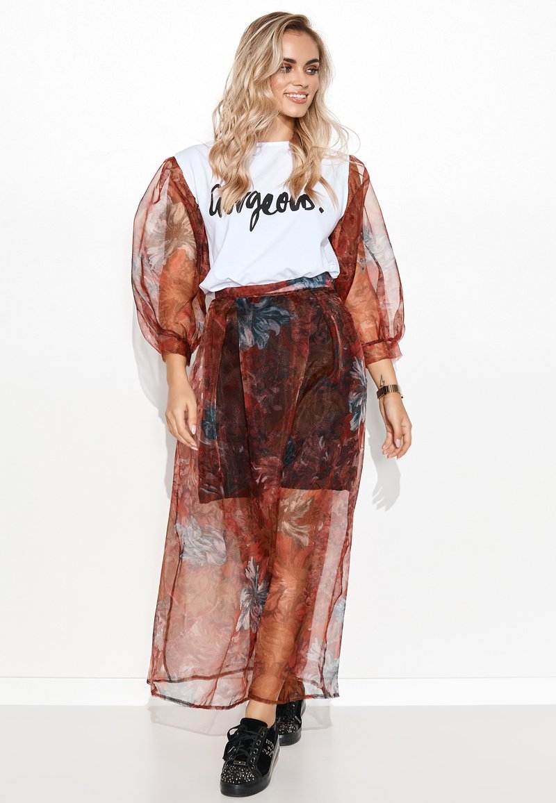 Przezroczysta, długa, czerwona spódnica w kwiaty z wysokim stanem, zestawiona z białym t-shirtem z czarnym napisem. Czarne, ozdobione sneakersy dopełniają całość.