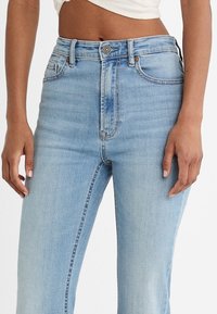 Lichtblauwe denim jeans met een hoge taille, vijf zakken en een rits met een metalen knoop. Vervaagde delen creëren een subtiele textuur.