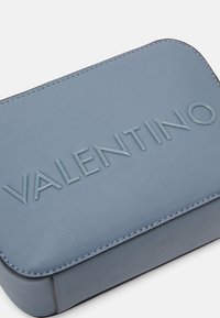Étui rectangulaire en cuir bleu avec logo "VALENTINO" embossé, texture lisse et couture subtile le long des bords.
