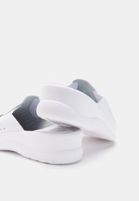 Vita slip-on skor med en jämn textur, rundad klack och en lätt upphöjning. Har perforeringar för andningsförmåga och en minimalistisk design.