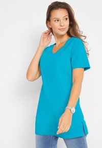 T-shirt turchese a maniche corte con scollatura a V e spacchi laterali. Realizzato in un tessuto morbido, presenta una vestibilità comoda e rilassata.