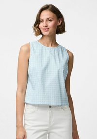 Svijetloplavi bezrukavac s teksturiranim uzorkom mreže, okruglim izrezom i ravnim krojem; uparen s bijelim trapericama.