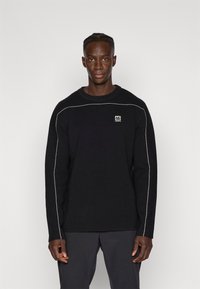 Maglione nero con collo a giro, caratterizzato da dettagli di cucitura bianca lungo le spalle e un piccolo patch del marchio sul petto.