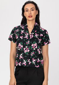 Chemise à manches courtes boutonnière en tissu noir avec un motif floral composé de fleurs roses et de feuilles vertes. Coupe ajustée, matériau léger.
