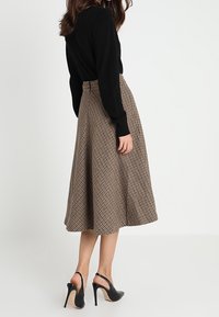 Ruskea houndstooth-kuvioinen midihame, jossa liehuva malli, korkea vyötärö ja joustava vyötärönauha, yhdistetty mustiin korkeakorkoisiin kenkiin.