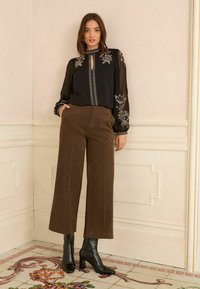 Crna prozirna bluzica s cvjetnim vezom i otvorom, uparena s smeškim širokim hlačama i crnim špicastim gležnjačama.