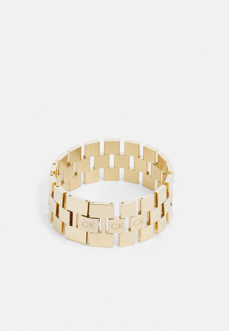 Pulsera de metal dorado que presenta eslabones rectangulares con la inscripción "CK" en secciones seleccionadas. Superficie lisa con un acabado pulido.