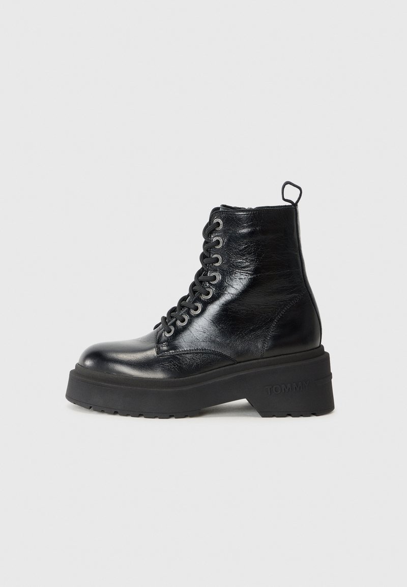 Bottine noire en cuir à lacets avec semelle en caoutchouc épaisse et languette au talon, embossée sur le côté avec « TOMMY » sur le bord de la semelle.