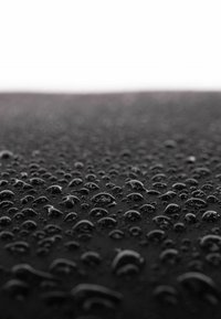 Superficie nera con numerose gocce d'acqua, che riflettono la luce, di varie dimensioni e che formano un pattern testurizzato su tutto il materiale.