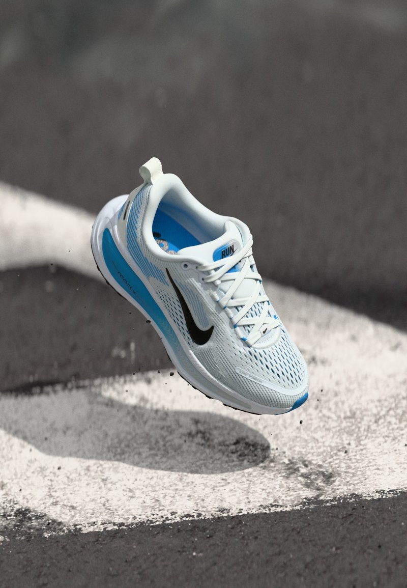 Nike běžecká obuv ve světle modré a bílé barvě s prodyšnou síťovinou, černým logem swoosh a texturovanými detaily na podrážce.