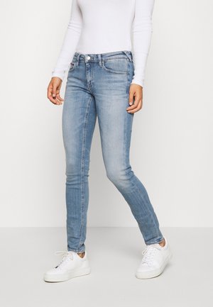 Vaqueros ajustados de color azul claro con un acabado desgastado, que cuentan con un bolsillo frontal, lazos para cinturón y una cremallera, combinados con zapatillas blancas.