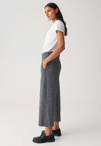Pantaloni grigi a gamba larga con una finitura in maglia testurizzata, dotati di tasche laterali, abbinati a una camicia bianca a maniche corte e scarpe nere.