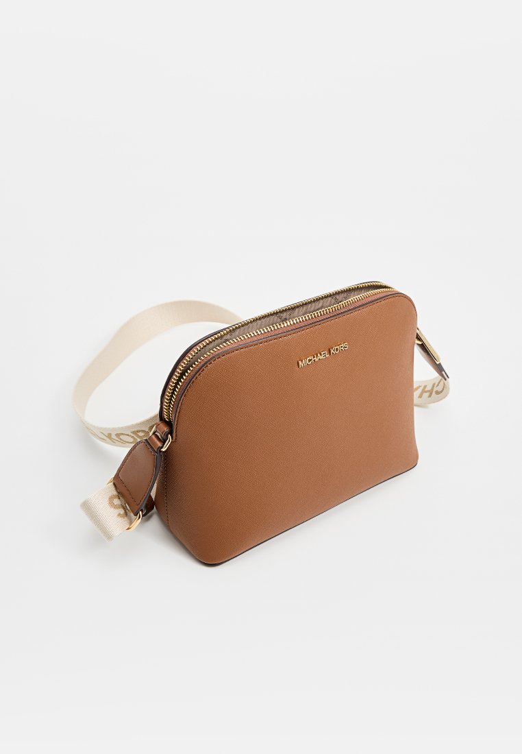 Sac bandoulière en cuir marron de forme ronde, avec des accessoires dorés et une sangle beige arborant un logo. Fermeture zippée en haut.