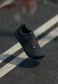 Scarpa da corsa nera con parte superiore in rete, texture perforata e suola ammortizzata. Presenta lacci e un profilo aerodinamico.