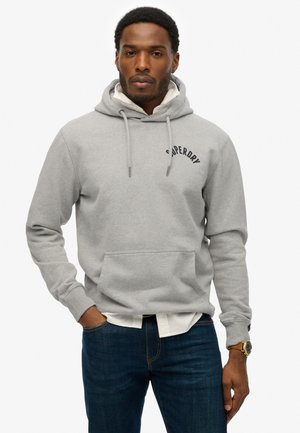 Grijze hoodie met trekkoorden en een voorkeurszak, met de tekst "Superdry". Draag het over een witte shirt, gecombineerd met donkerblauwe jeans.