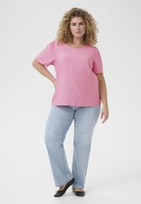 Top rosa a maniche corte con scollatura tonda, abbinato a jeans dritti blu chiaro e scarpe basse nere. Tessuto liscio, design casual.