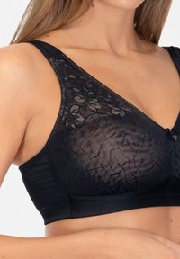Czarny biustonosz z przezroczystą koronkową górą z kwiatowymi wzorami, gładkim pasem, szerokimi ramiączkami i małą kokardką na środku.