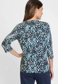 Bunt gemusterte Bluse mit schwarzem Hintergrund, blauen und weißen abstrakten Mustern, 3/4-Ärmeln und Rundhalsausschnitt. Weiche Textur.