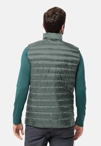Gilet grigio isolato con colletto alto, caratterizzato da un design trapuntato e una texture liscia. Indossato su una maglietta a maniche lunghe color teal.