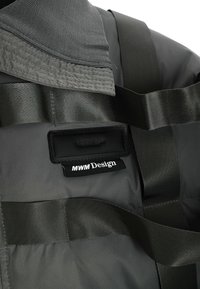 Tela técnica gris con un cuello acolchado, correas negras prominentes y etiquetas que muestran "MWM Design" con una textura suave.