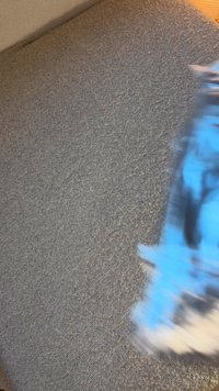 Teksturirana sivka tkanina z zamegljenim modrim predmetom, ki ga delno prekriva, kar poudarja njegovo barvo in obliko na ozadju.