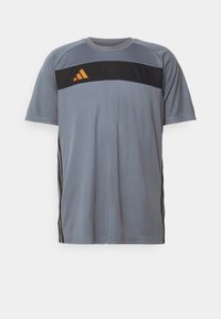 Šedé sportovní tričko vyrobené z prodyšného materiálu, s černým vodorovným pruhovaním a oranžovým logem, a černými bočními panely.