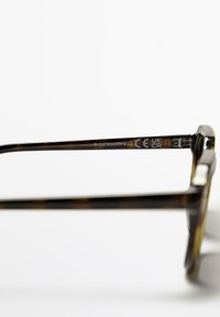 Occhiali da sole tortoise brown con un design elegante e piatto. La montatura presenta marchi CE e UKCA in rilievo sulla tempia.