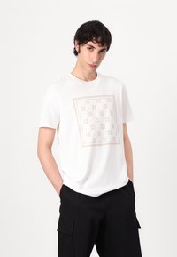 Camiseta blanca de manga corta con un patrón geométrico en tono claro en un marco cuadrado. Hecha de una tela suave, corte holgado y diseño de cuello redondo.