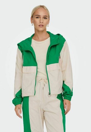 Color-blocked jacket featuring a green top and light beige bottom, with a hood, zip closure, and elastic cuffs. Smooth fabric texture.