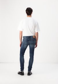 Slim-fit blå denimjeans med bakfickor, subtil blekning och en brun läderlapp på midjan. Matchas med en loose white t-shirt.