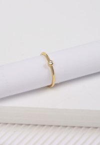 Gouden ring met een gepolijste afwerking, met een enkele heldere edelsteen in een ronde verpakking. Weergegeven tegen een lichte achtergrond.