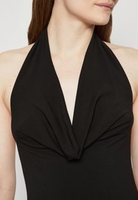 Black halter-neck swimsuit featuring a deep V-neckline with gathered fabric at the chest, made from smooth, stretchy material.