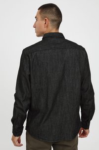Črna denim srajca z teksturirano površino, z gumbi na manšetah in klasičnim ovratnikom. Hrbtna stran ima šiv v obliki jame za dodaten detalj.