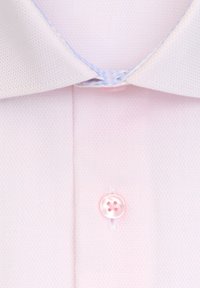 Gros plan sur une chemise texturée rose pâle montrant le col et le premier bouton fermé avec un bouton assorti.