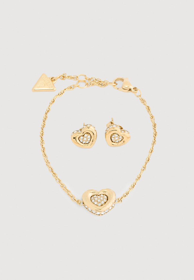 Ensemble de bijoux dorés comprenant un bracelet en forme de cœur et des boucles d'oreilles, ornés de strass transparents et d'un design en chaîne torsadée.