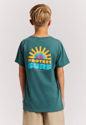 T-shirt en coton bleu sarcelle avec un col rond. Le dos présente un graphisme coloré d'un soleil, avec les mots "PROTEST" et "SURF" en nuances de jaune et de bleu.
