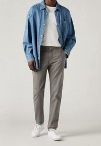 Denimskjorta i ljusblått, vit t-shirt med rund hals, grå byxor och vita sneakers. Har en knappslutning och en framficka på skjortan.