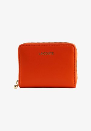 Portefeuille en cuir orange avec fermeture éclair et tirette dorée, portant le logo "LACOSTE" centré sur le devant.