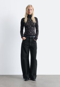 Black floral long-sleeve turtleneck top paired with oversized black trousers. The outfit features a thin black belt and tapered shoe design.