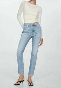 Top ajustado de manga larga en amarillo claro combinado con jeans de mezclilla azul claro de cintura alta. Corte slim y pierna recta, con sandalias negras de tacón.