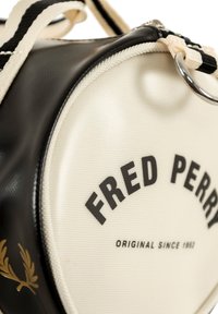 Sort og creme farvet stof duffel bag med rund form, prydet med logo print og gyldne laurbær accenter. Inkluderer sorte og creme stribede remme.