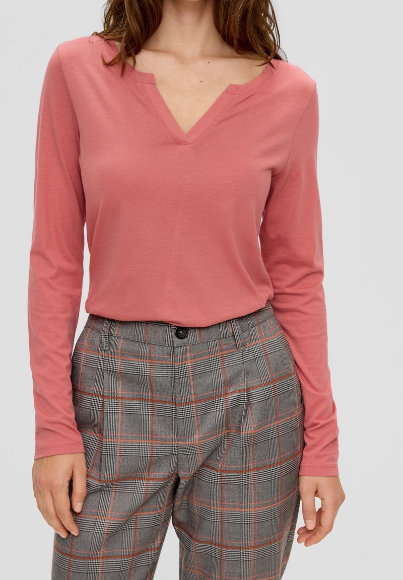 Långärmad, v-ringad topp i korallrosa bomull, i kombination med grå rutiga högmidjade byxor med röda detaljer och knappstängning.