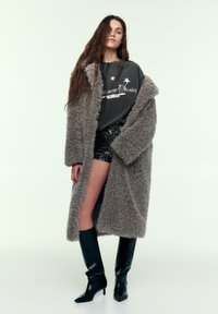 Oversized grå faux fur-frakke med shawl-krave, kombineret med en sort palietkort nederdel og knæhøje sorte spidse støvler.