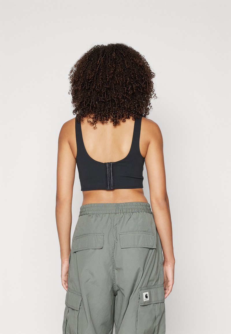 Reggiseno sportivo nero con spalline larghe e schiena a barchetta, dotato di chiusura a gancio e occhiello. Abbinato a pantaloni cargo verde oliva con tasche.